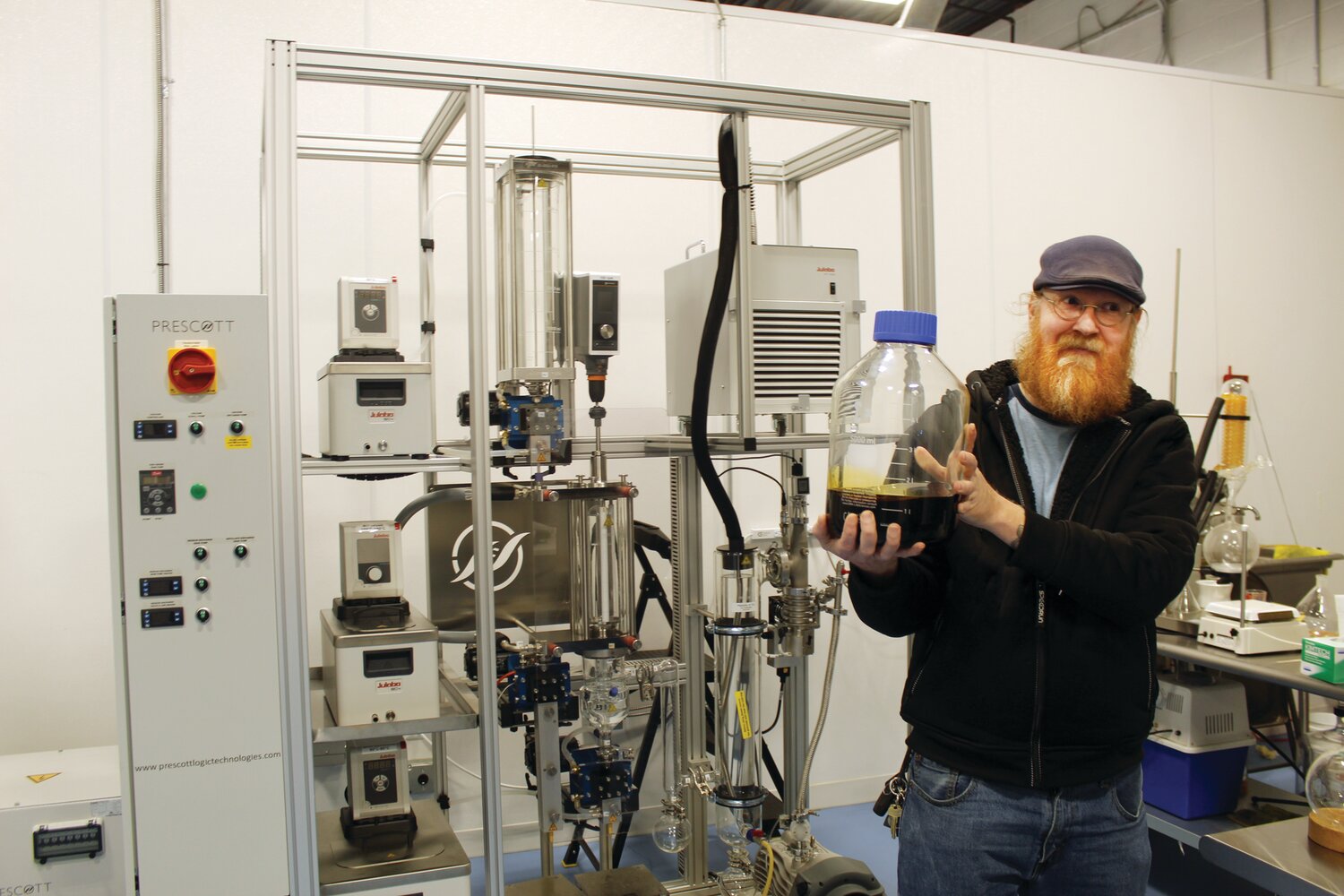 Jason Carlson holds up a bottle of THC distillate, created at Hapi using the CO2 powered extraction device behind him. The extract is used to create number of adult-use spinoffs of popular local brands, including Del's Lemonade and the Original Italian Bakery's pizza chips.